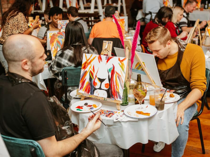 Two men sit opposite one another at a sip and paint event